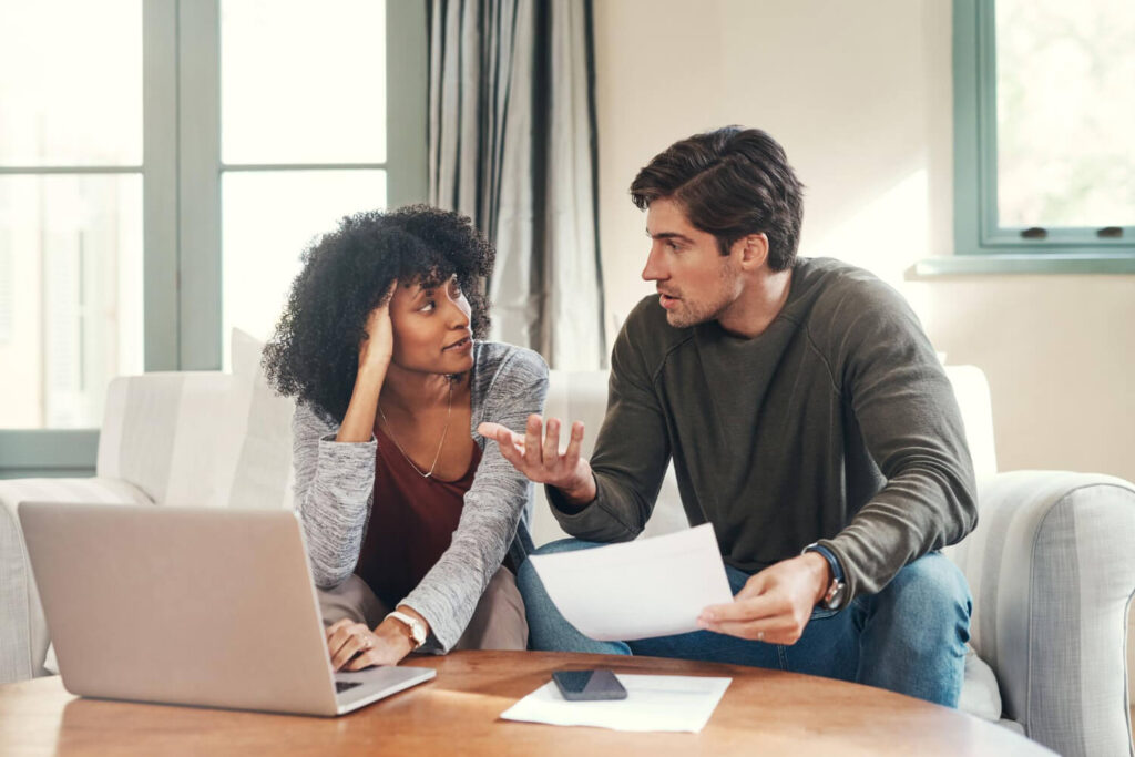 Couple en désaccord devant une maison avec des documents juridiques sur une table