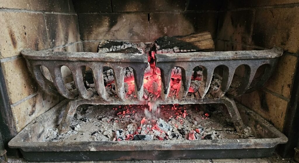 Grille de décendrage en fonte fendue en deux au fond d'un insert de cheminée, laissant tomber les braises.
