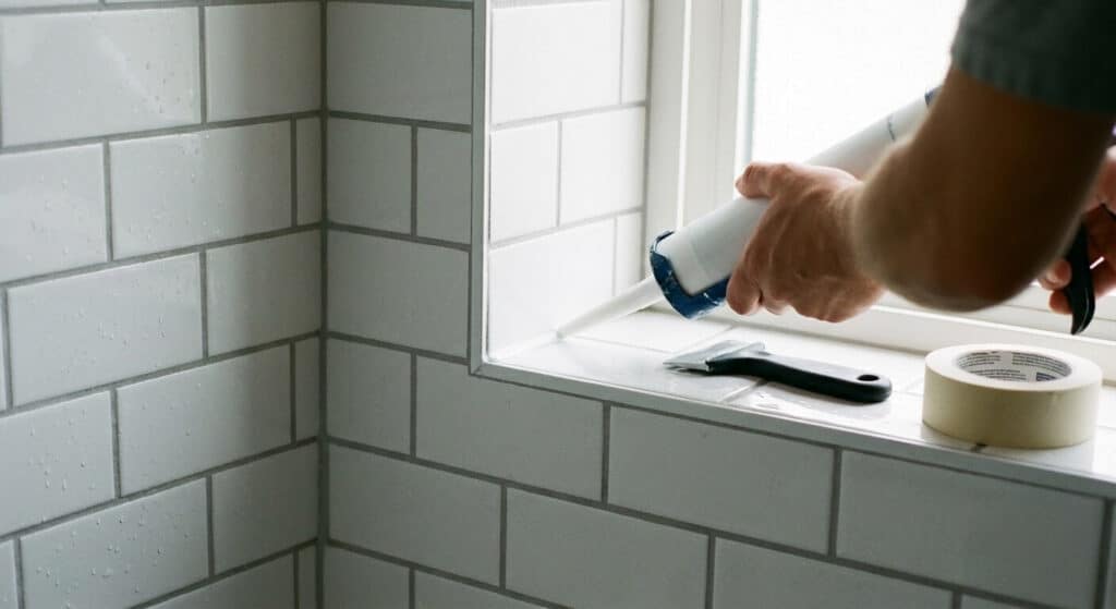 Application d'un joint silicone blanc dans l'angle d'une douche carrelée pour assurer l'étanchéité.