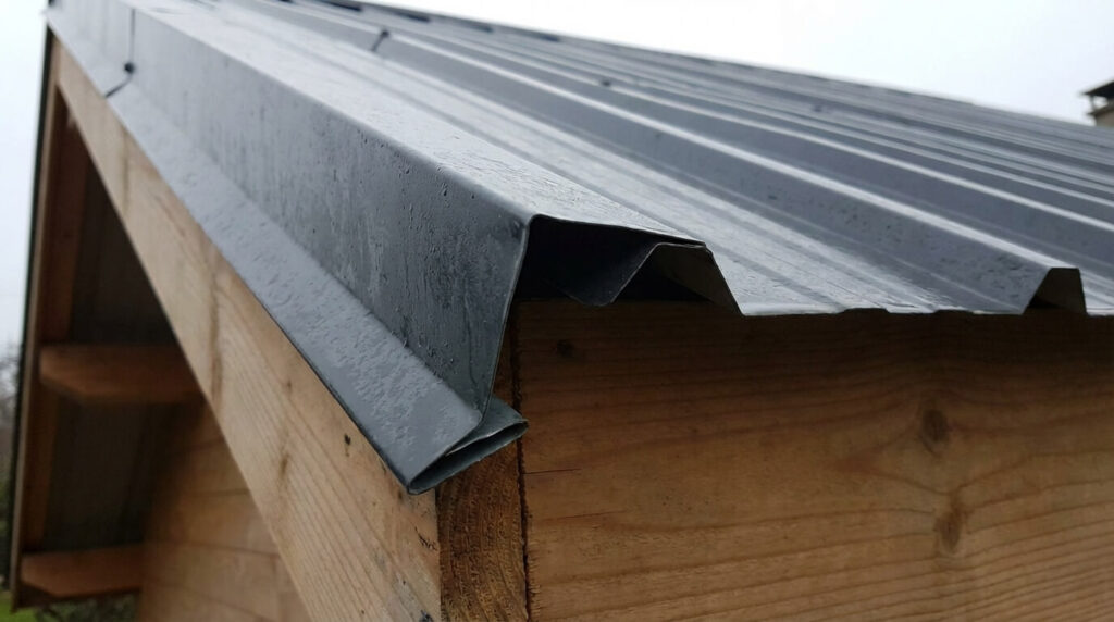Débord de toiture bac acier dans la gouttière : Quelle distance respecter ? 2 Détail d'une tôle bac acier avec l'extrémité pliée vers le bas (cassure de goutte) pour éviter la remontée d'eau par capillarité sous la toiture