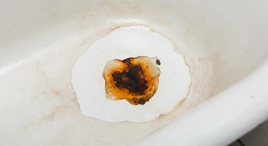 Éclat d'émail laissant apparaître une tache de rouille au fond d'une baignoire ancienne
