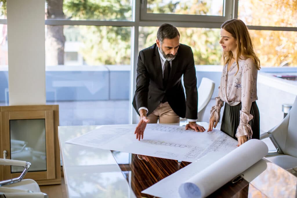 Un architecte et un commerçant examinant les plans de rénovation d'une boutique pour anticiper les risques techniques.