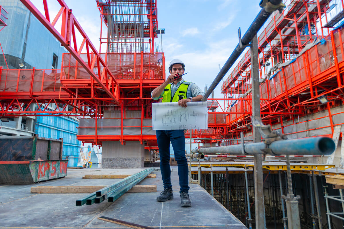 Portrait d'un ingénieur en génie civil souriant, tenant les plans d'exécution d'un plancher en béton pour un chantier de construction.