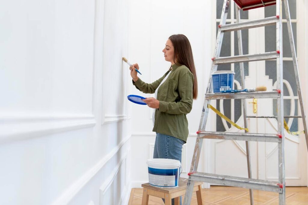 Un locataire peignant un mur en blanc pour rénover le salon de son logement en location.